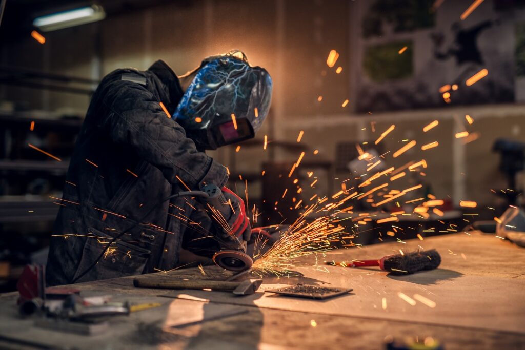 Craftsman sawing metal, sparkles around workshop.