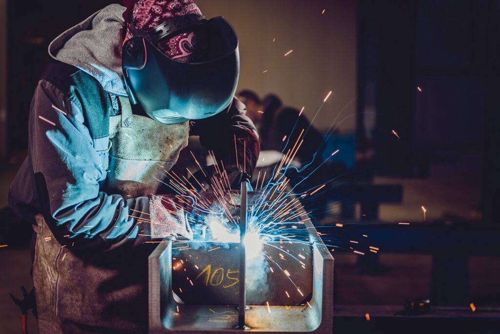 Industrial Welder With Torch and Protective Helmet in big hall welding metal profiles
